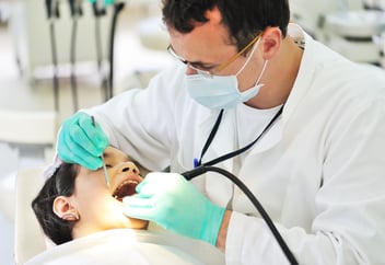 dentist with gloves on using instrument in patient's mouth