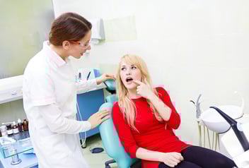 dentist standing beside a patient pointing at her mouth