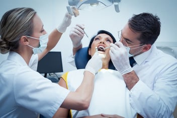 two dentists holding instruments over a female patient