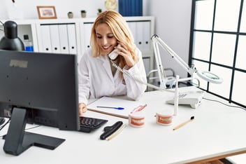 female dentist sitting in front of laptop on the phone