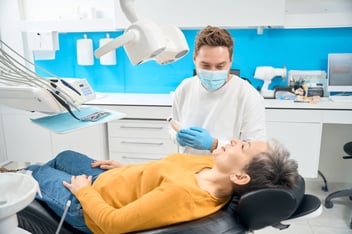 male dentist with a mask on looking at a female patient in the dental chair