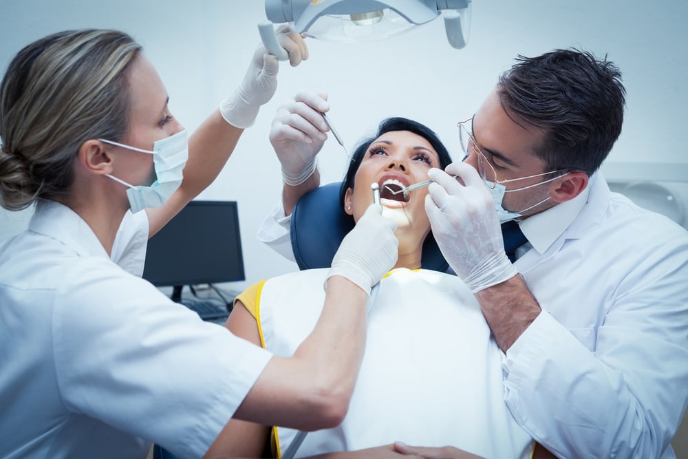 two dentists holding instruments over a female patient