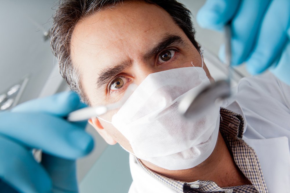 Dentist standing over patient holding a dental instrument