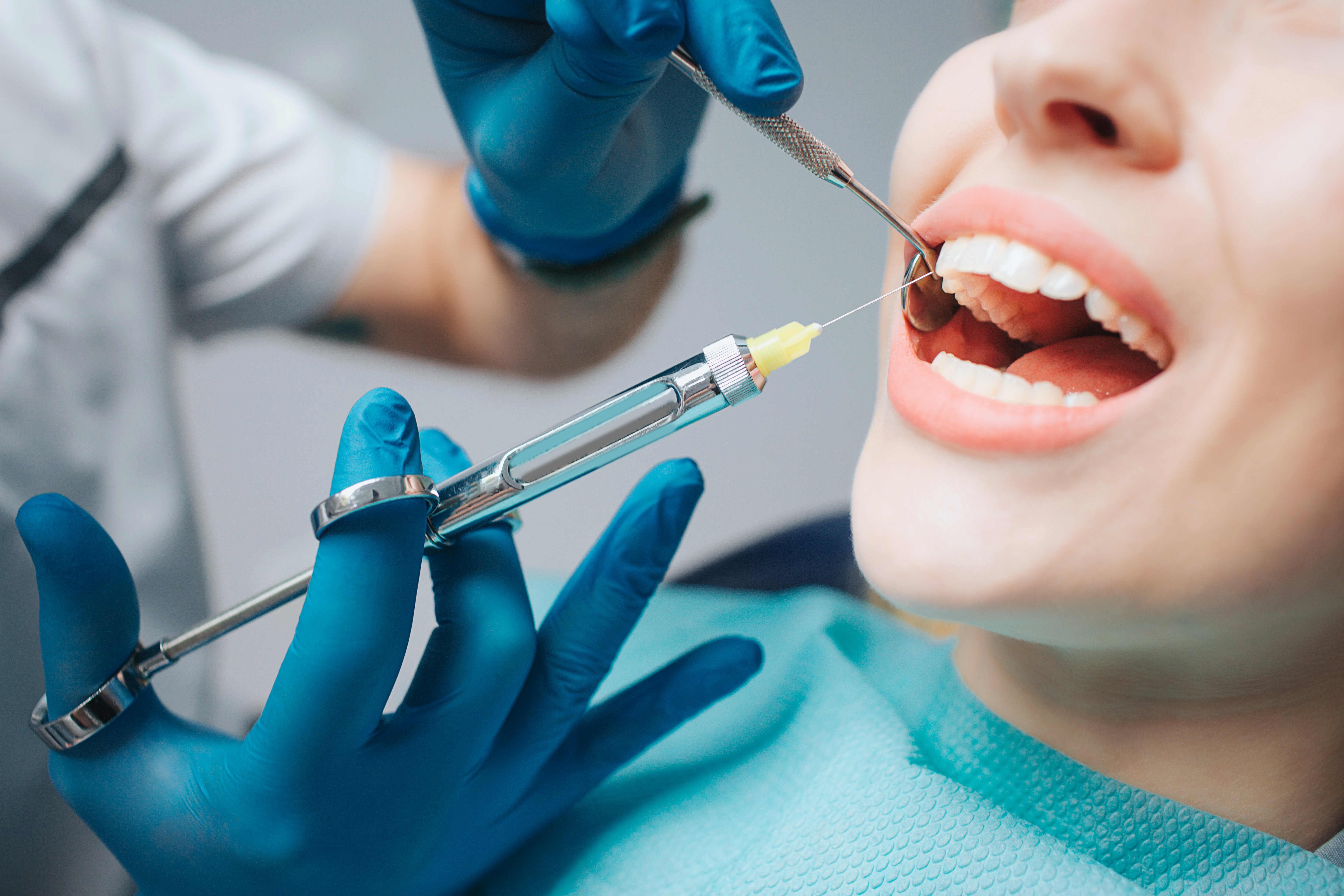 hands in medical gloves holding a needle to a patient's mouth