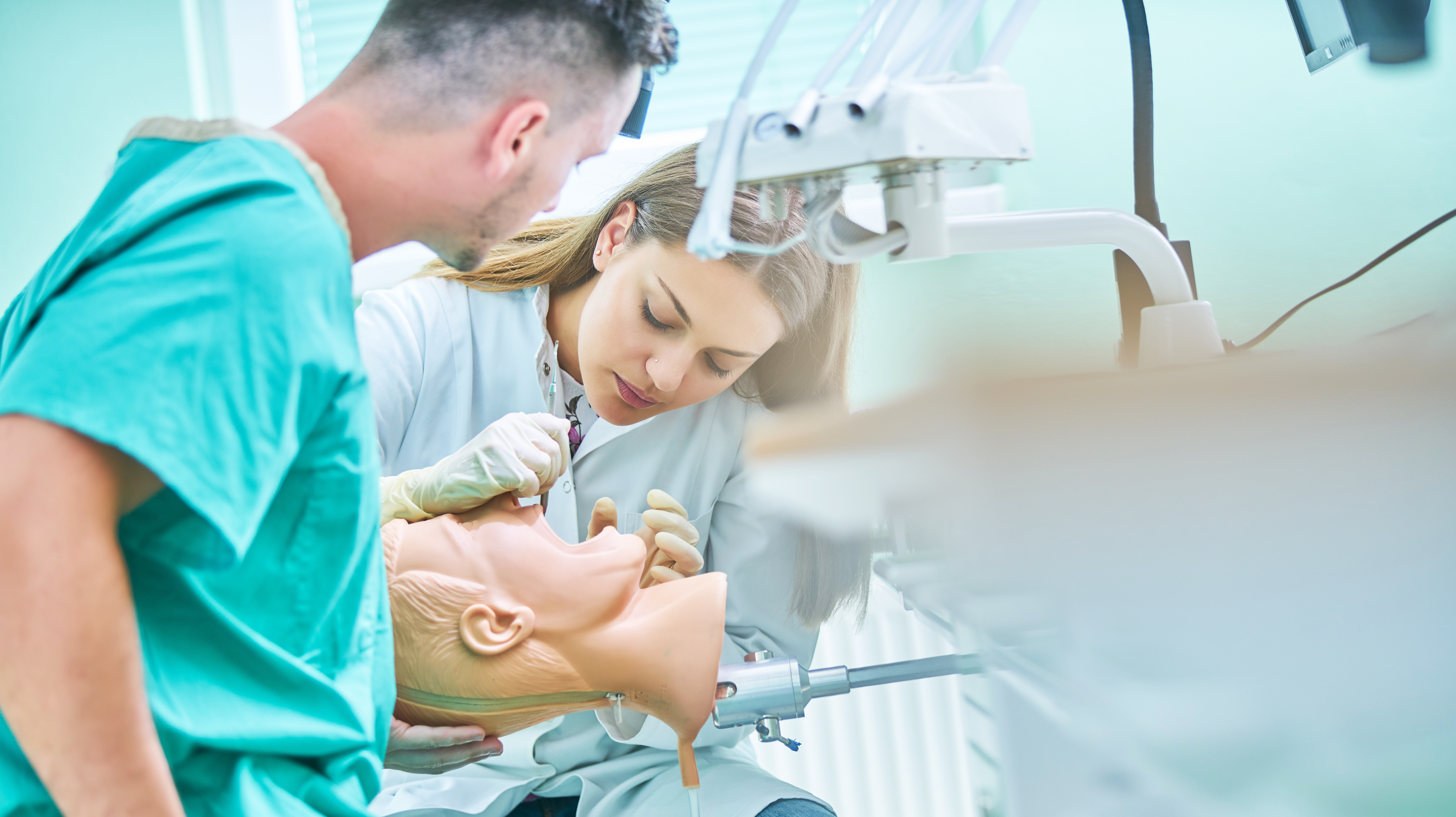 Dental mentor observes as dental student practices on training manikin.