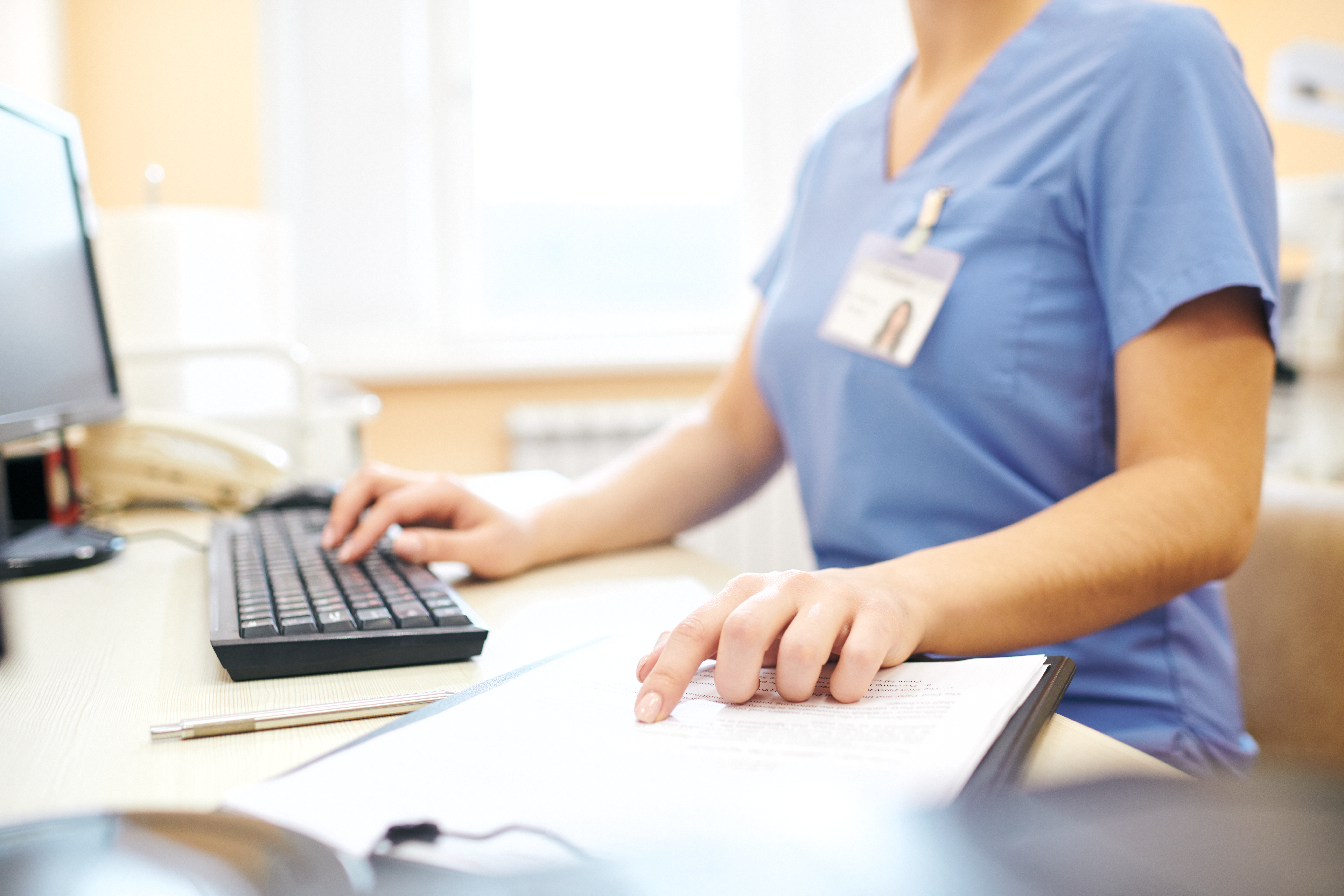 healthcare provider at a computer with a keyboard and taking notes